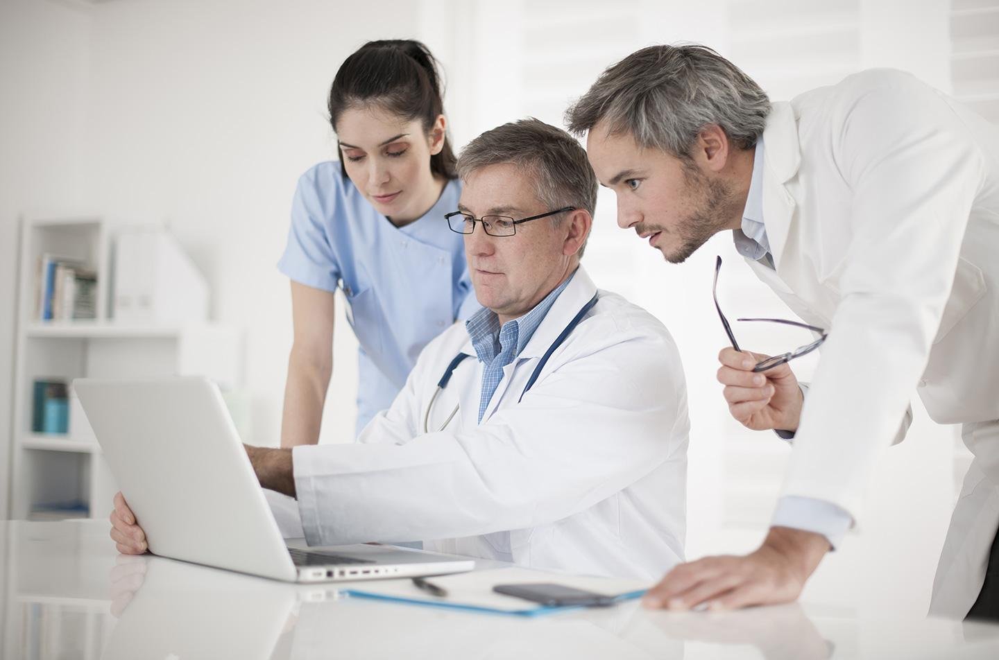 Tres profesionales de la salud revisando juntos una computadora portátil en un consultorio